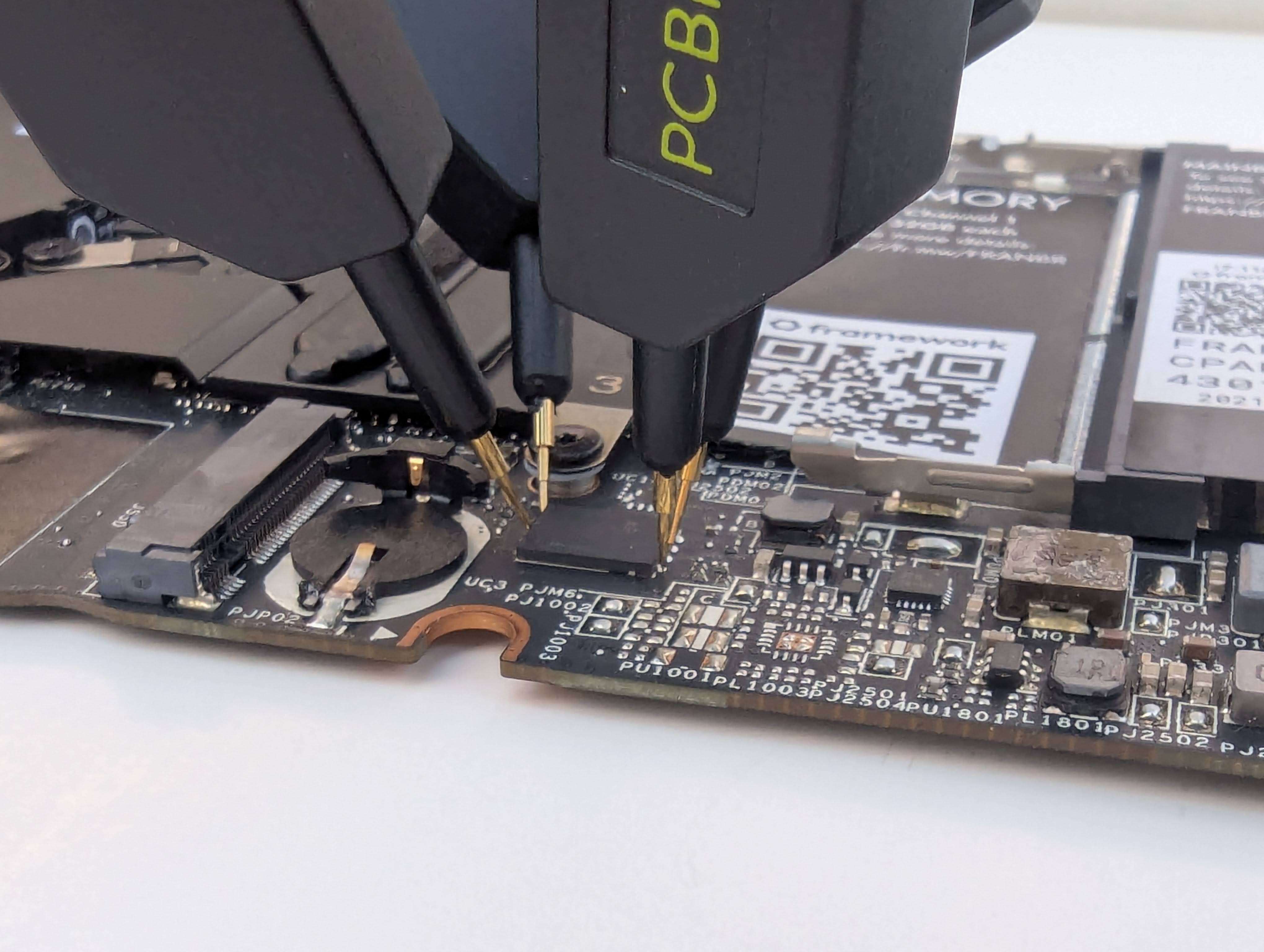 Photo showing a laptop motherboard with logic analzer probes connected to a flash rom chip